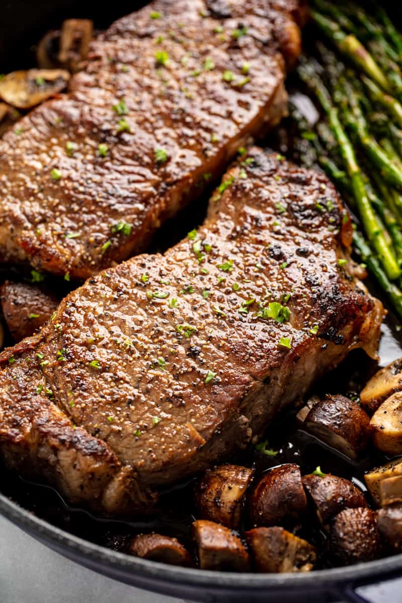 Close up of Skillet Steak with Asparagus and Mushrooms in a cast-iron skillet.