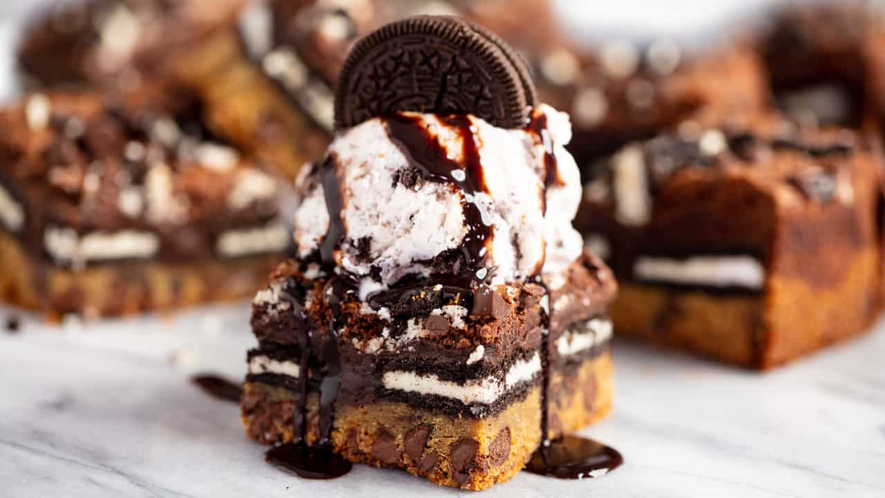 Close up of Slutty Brownies topped with a single scoop of vanilla ice cream and one whole Oreo cookie and drizzled with chocolate syrup.