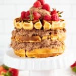 Waffle Cake on a cake stand surrounded by strawberries.