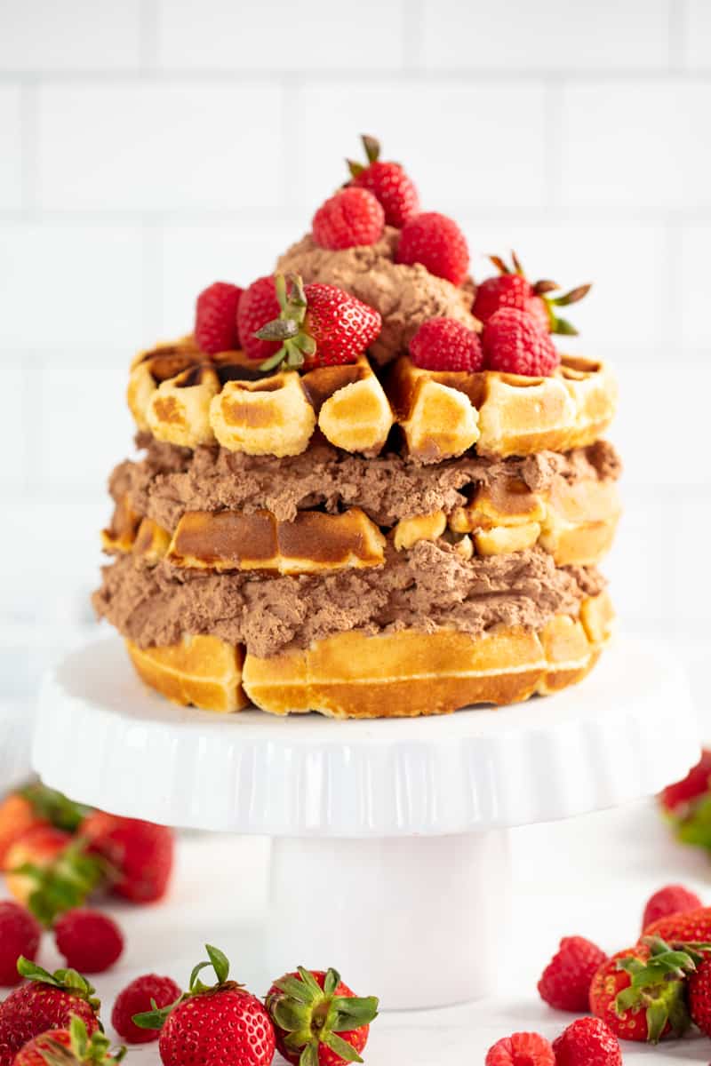 Waffle Cake on a cake stand surrounded by strawberries.