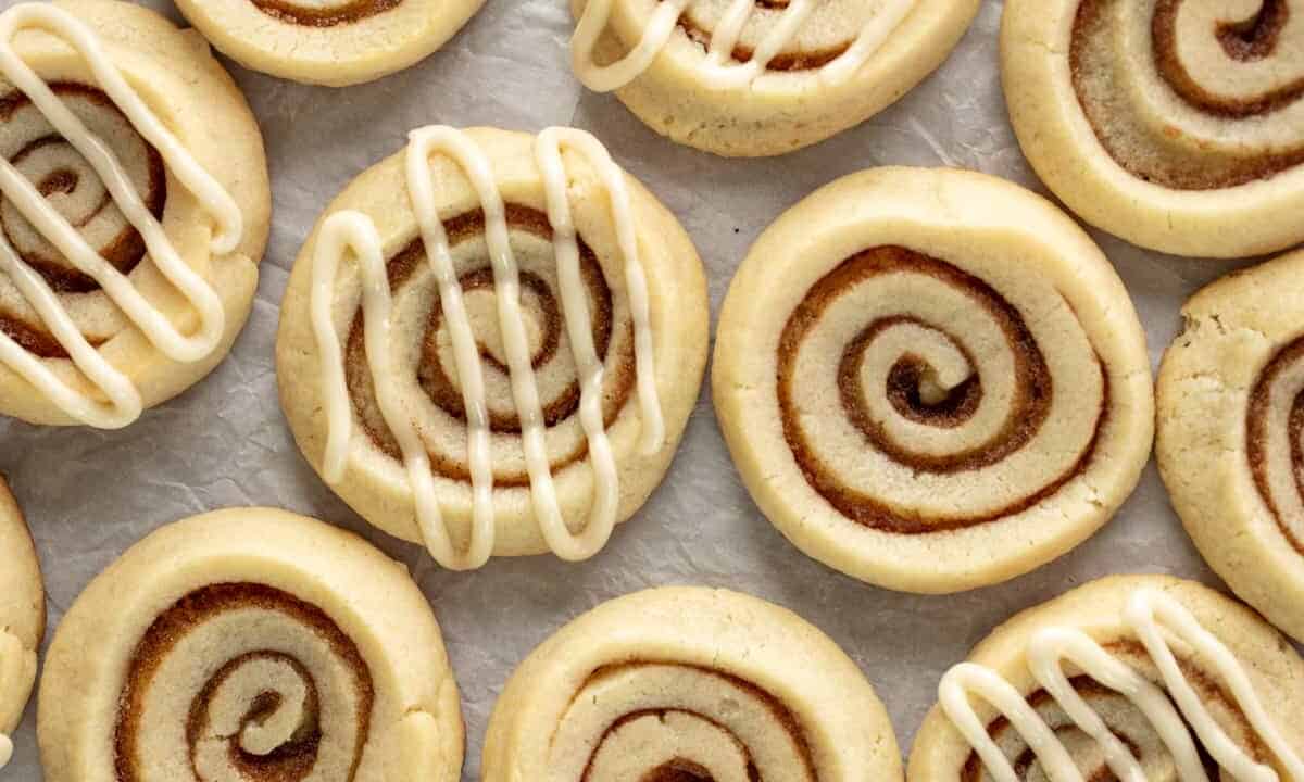 Cinnamon roll cookies layed out on parchment paper, some with frosting drizzle, some without.