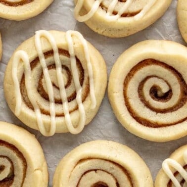 Cinnamon roll cookies layed out on parchment paper, some with frosting drizzle, some without.