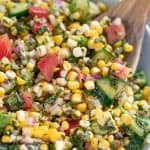 Corn salad in a white bowl with a wooden spoon in it.