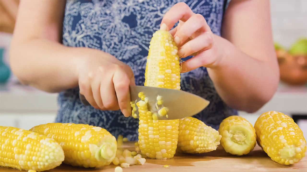 Using kitchen knife remove corn kernels from cob after boiling on cutting board