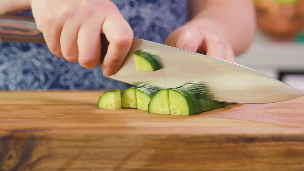 Using Kitchen Knife quarter cucumbers on cutting board.