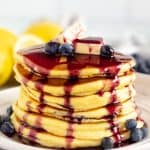 A stack Lemon Ricotta Pancakes covered with syrup and topped with berries and butter.