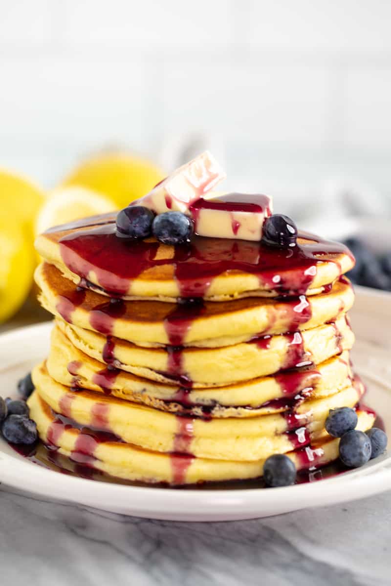 A stack Lemon Ricotta Pancakes covered with syrup and topped with berries and butter.