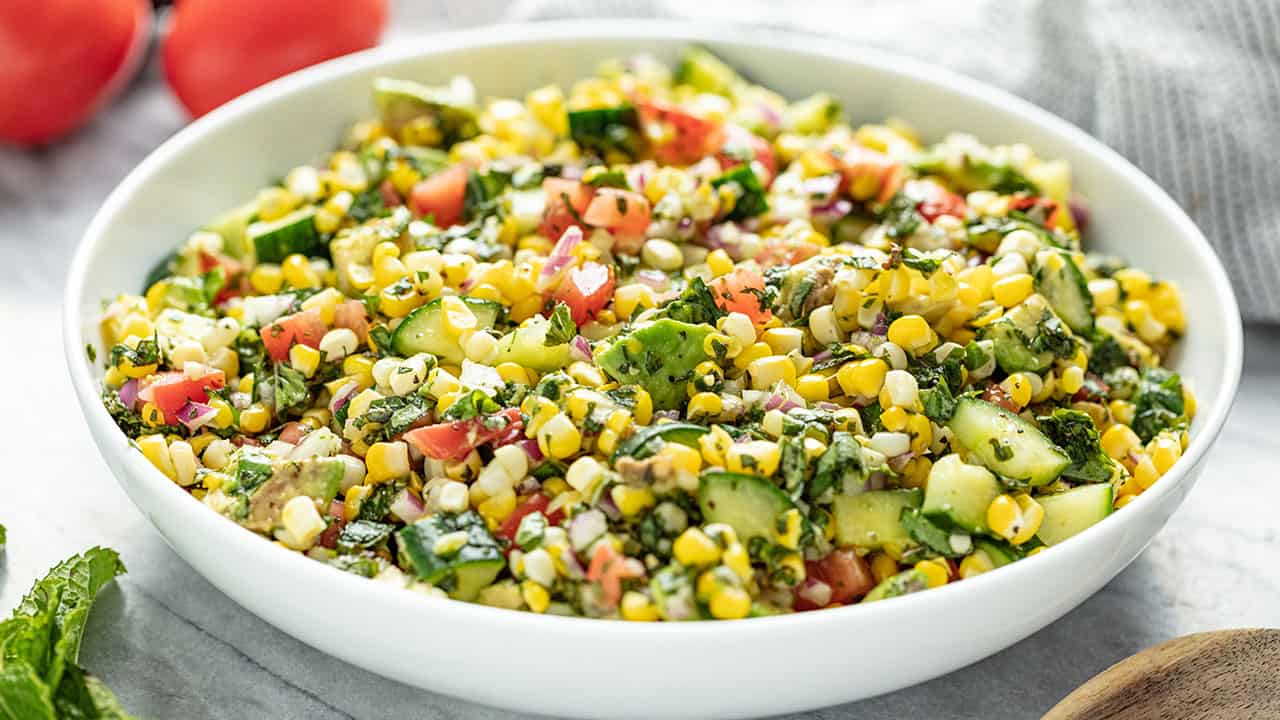 Fresh Corn Salad in a white bowl setting on a marble countertop.