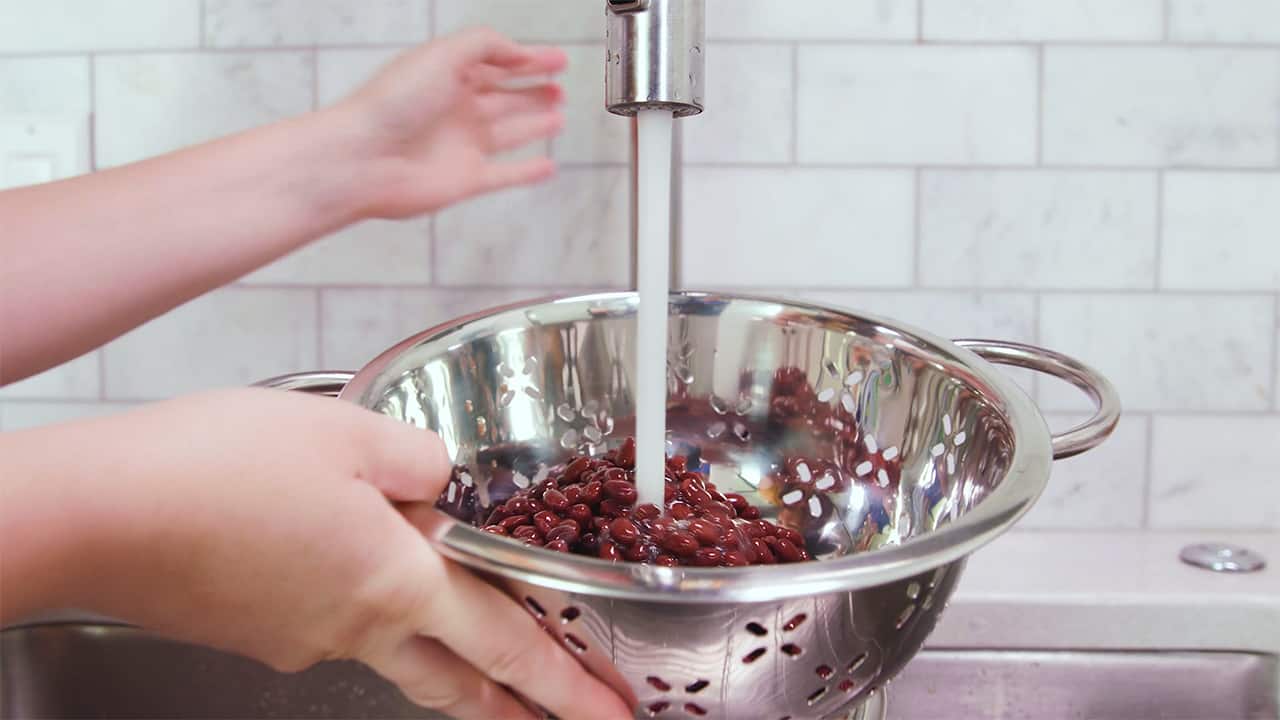 Using water faucet, thoroughly rinse black beans in metal colander over sink.