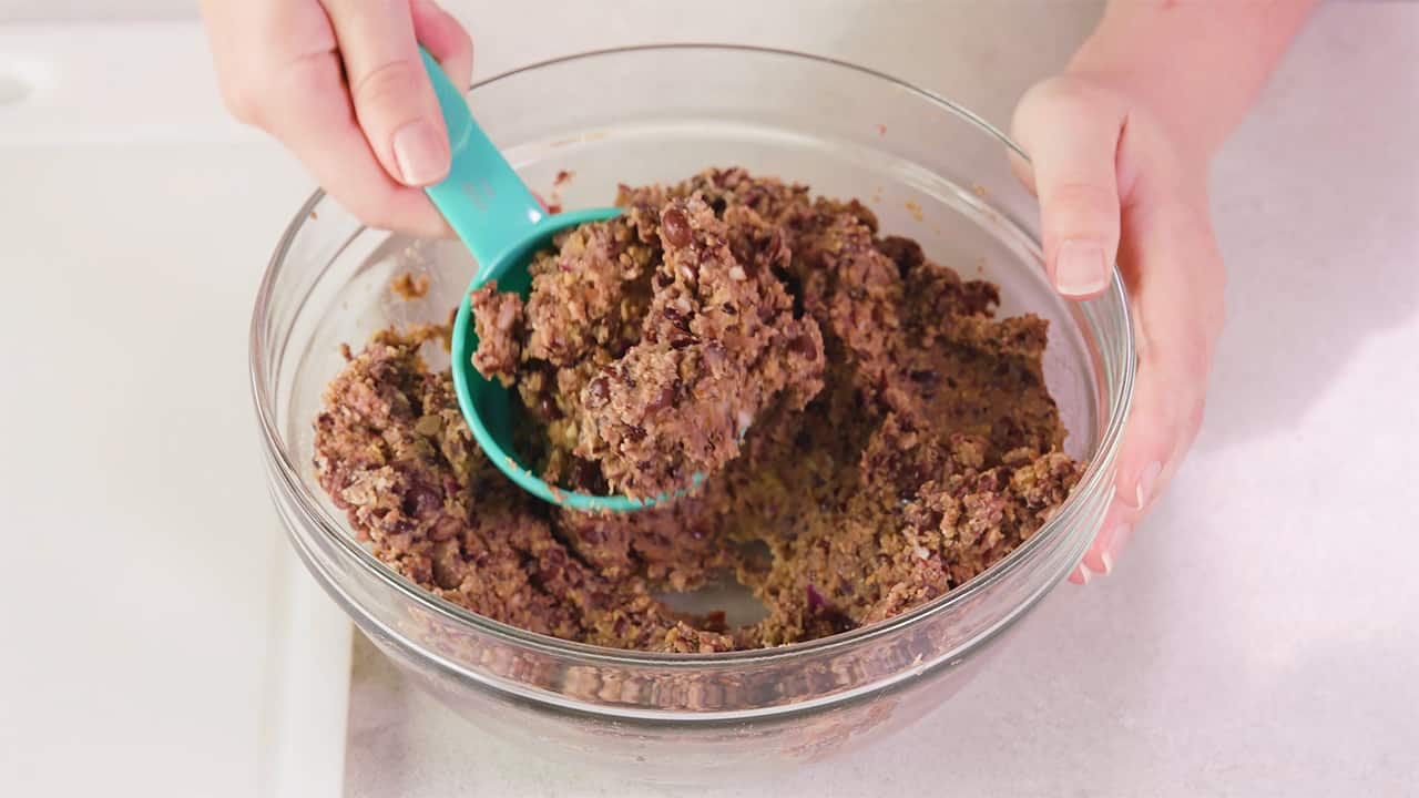 Using a half cup measuring cup, portion out the black bean burger mix from a medium size mixing bowl into patties.