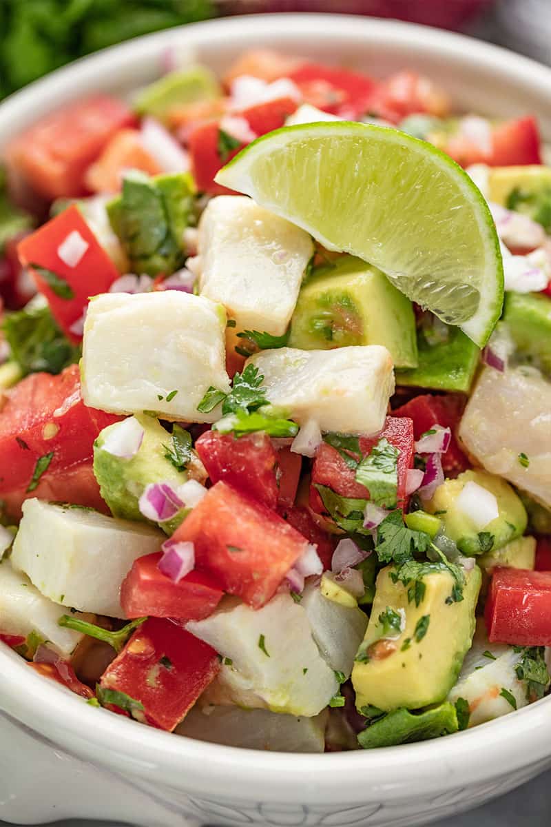 Close up of Ceviche topped with a lime wedge in a white bowl.