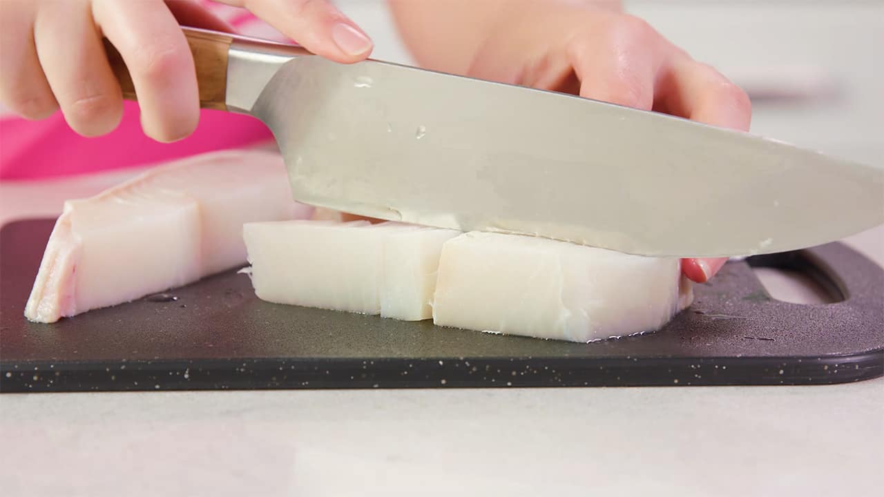Use sharp kitchen knife to cube white fish into bite sized portions on a cutting board.