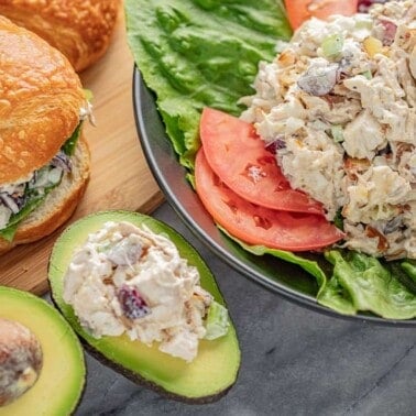 Three different applications of Chicken Salad; On a croissant sandwich, on blue plate garnished with lettuce and tomato, and stuffed into an avocado.