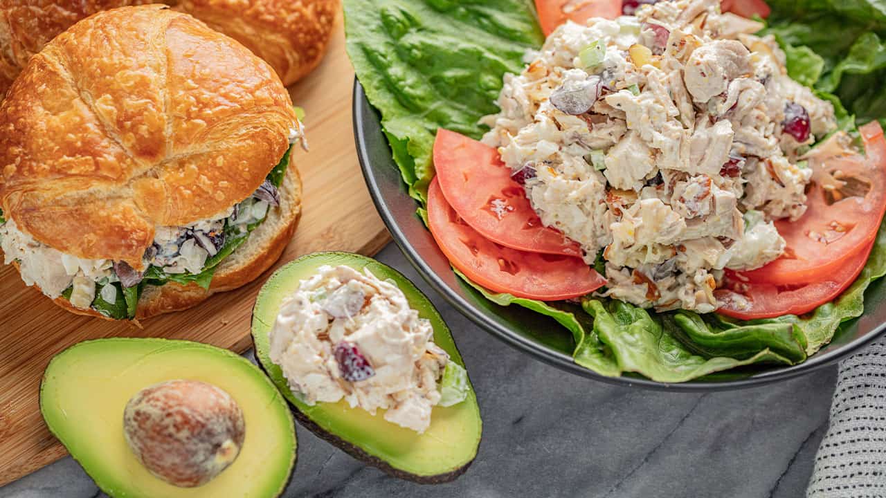 Three different applications of Chicken Salad; On a croissant sandwich, on blue plate garnished with lettuce and tomato, and stuffed into an avocado.