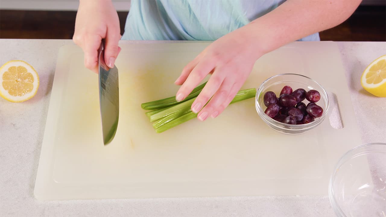 Using Kitchen Knife on cutting board chop halved celery stalks.