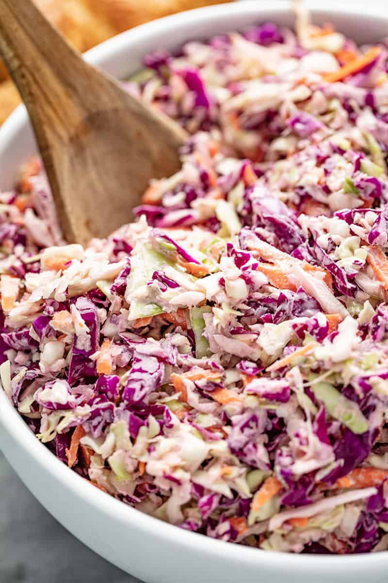 Coleslaw in a white bowl with a wooden spoon in it.