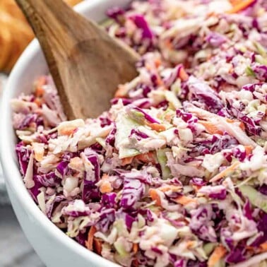 Angled view of a full bowl of Coleslaw served with a wooden spoon.