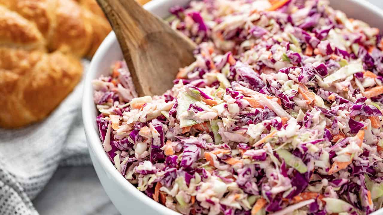Angled view of a full bowl of Coleslaw served with a wooden spoon.