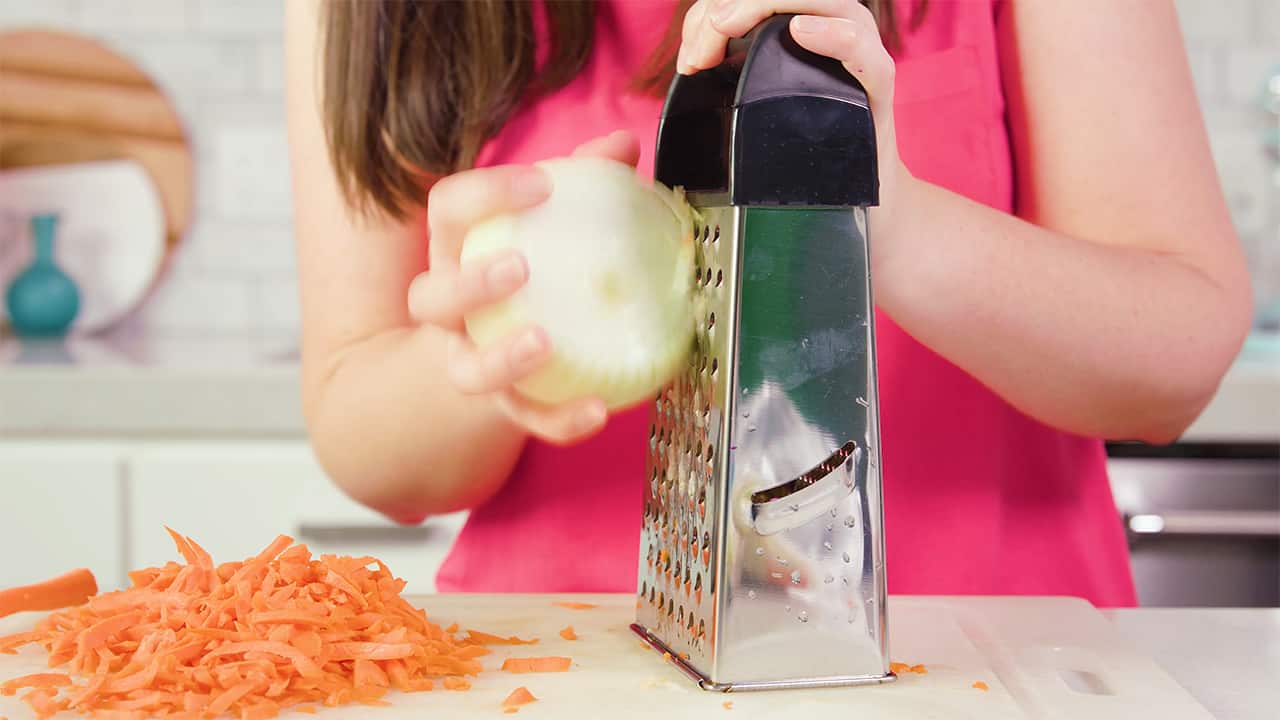 Using cheese grater on cutting board, slice onion and carrots to desired amounts.