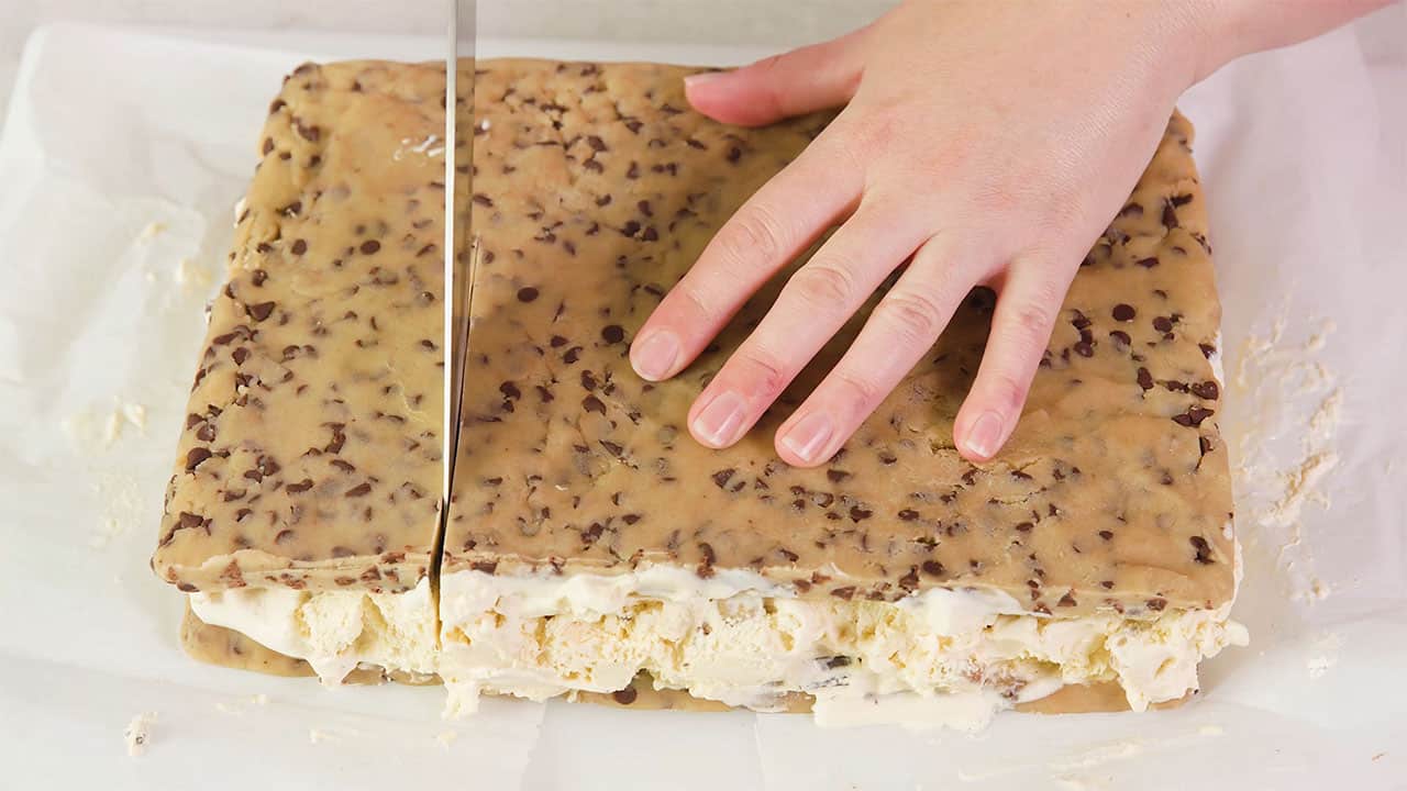 Overhead view of the sandwiched layers of chocolate chip cookie dough with vanilla ice cream in the middle and a kitchen knife cutting into the block to make individual servings.