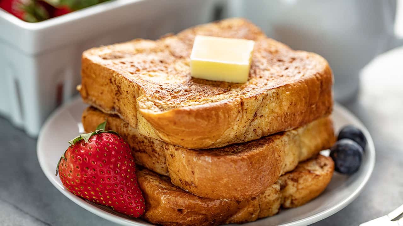 A stack of French Toast with a pad of butter on it all on a white plate garnished with berries.