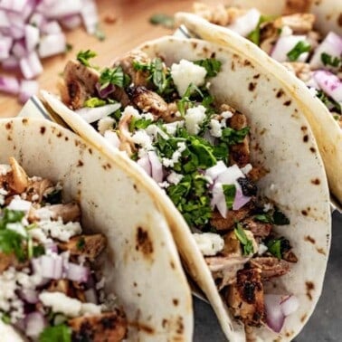 Close up of Grilled Chicken Tacos garnished with red onion and cilantro in a taco holder.