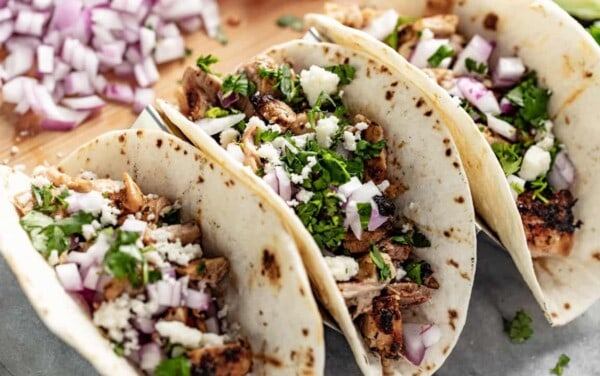 Close up of Grilled Chicken Tacos garnished with red onion and cilantro in a taco holder.