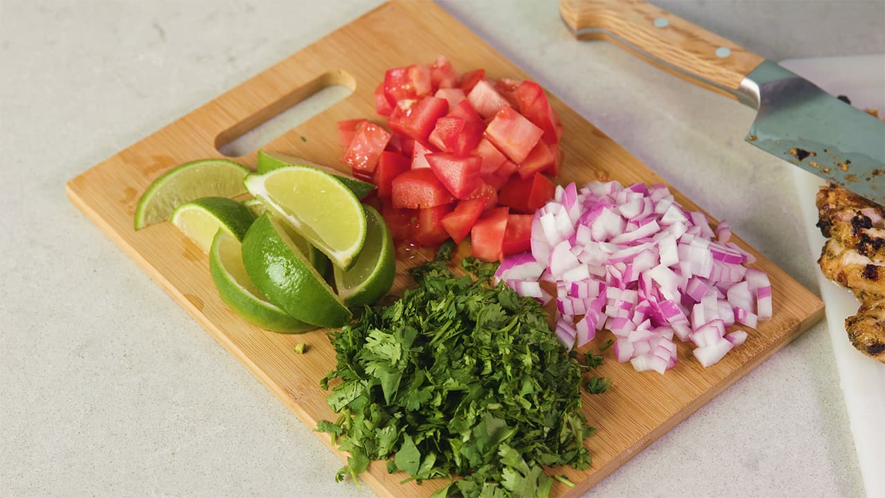 On a cutting board prepare garnishes by chopping tomatoes, onions and cilantro into desired portions and quarter limes for a splash of added flavor.