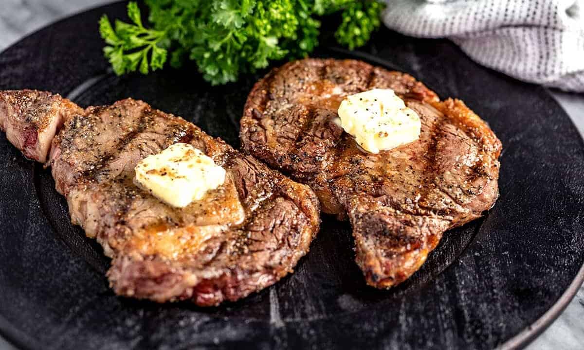 Angled view of Grilled Steak with a pad of butter on top served on a black plate.