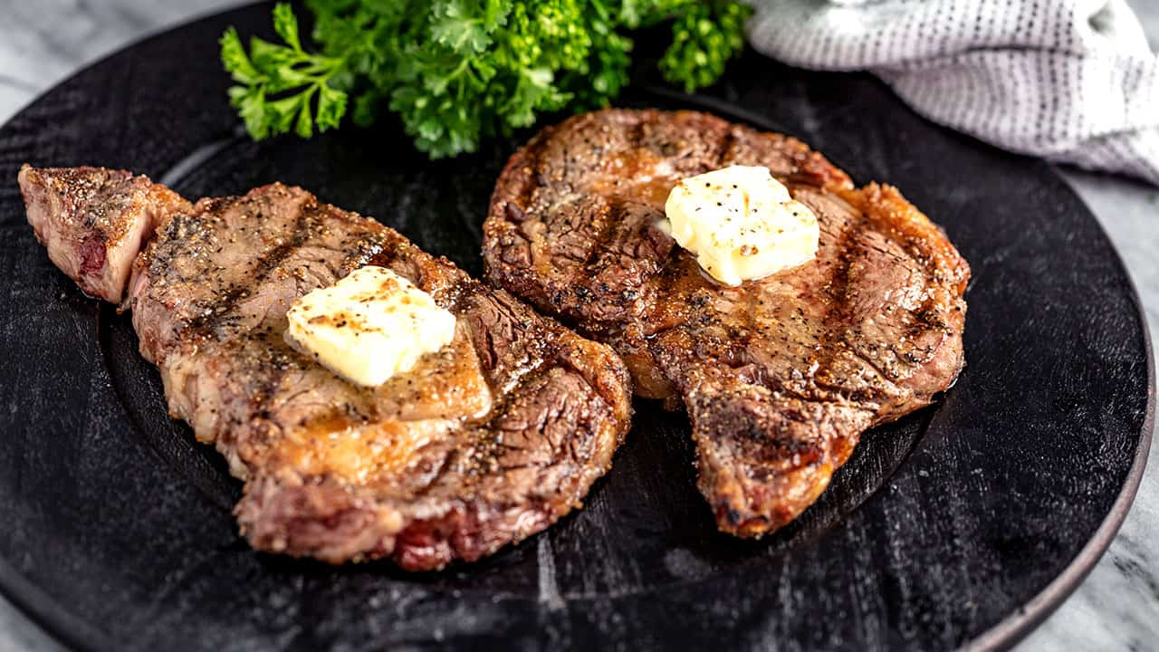 Angled view of Grilled Steak with a pad of butter on top served on a black plate.