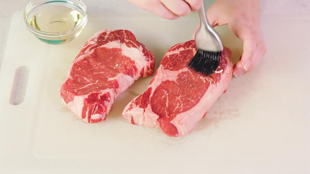 Using basting brush, rub the raw steak with oil on cutting board.