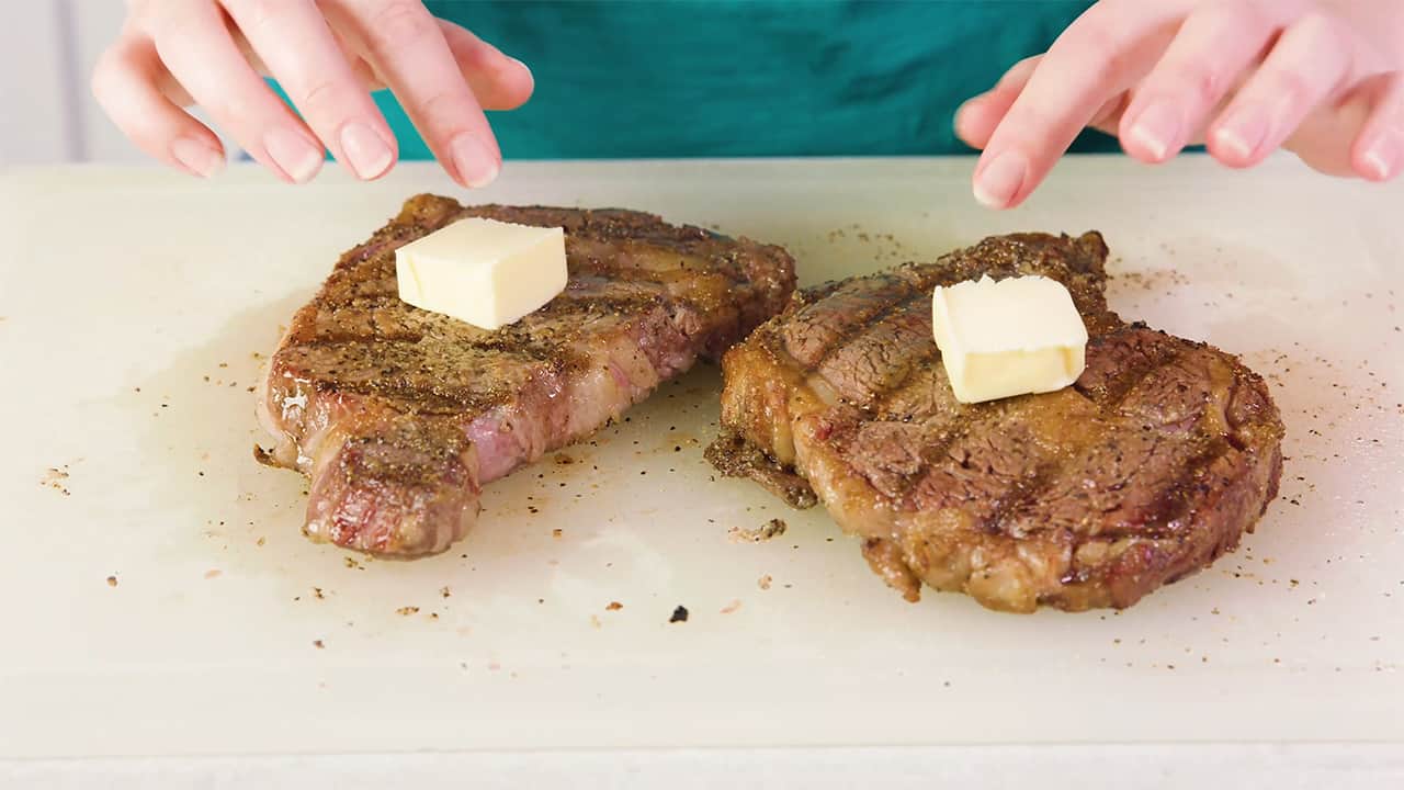 Once removed from grill top each of the two cooked steaks with a tab of butter while setting on a cutting board.