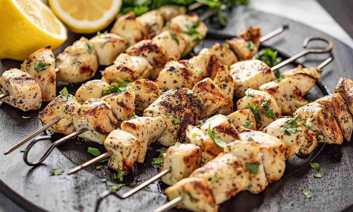 Lemon Chicken Kabobs garnished with lemon halves and parsley on a black plate.