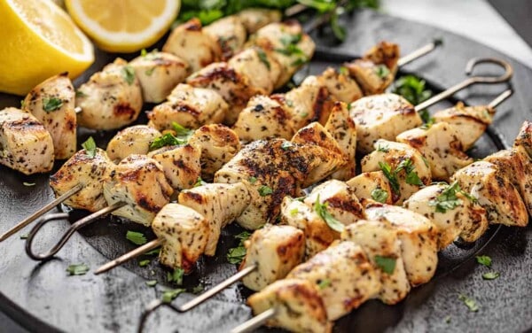 Lemon Chicken Kabobs garnished with lemon halves and parsley on a black plate.