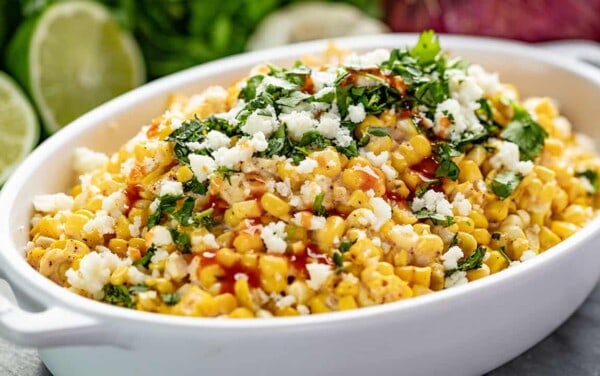 Angled view of Mexican Street Corn Salad in a white dish drizzled with hot sauce.