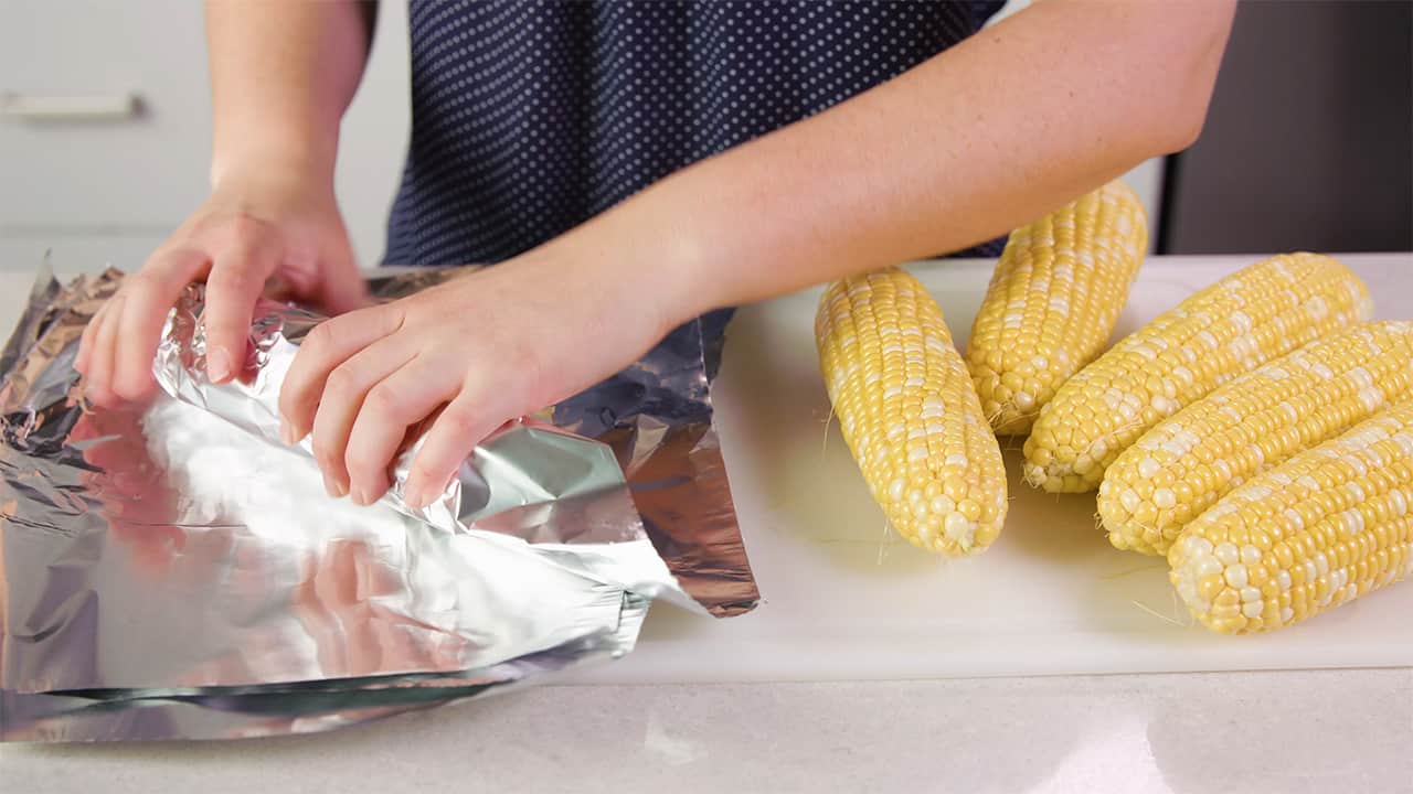 Using aluminum foil squares, wrap each corn cob with foil working on cutting board.