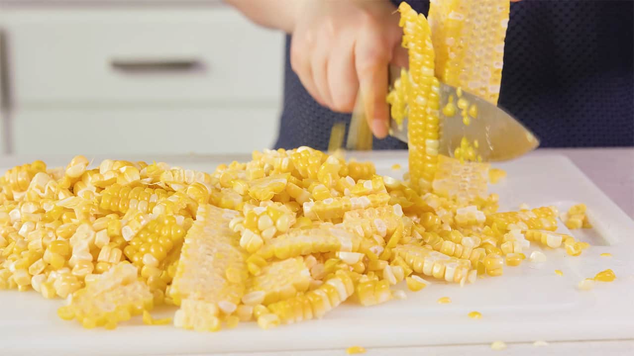 Using a kitchen knife, remove corn kernels from cob on cutting board.