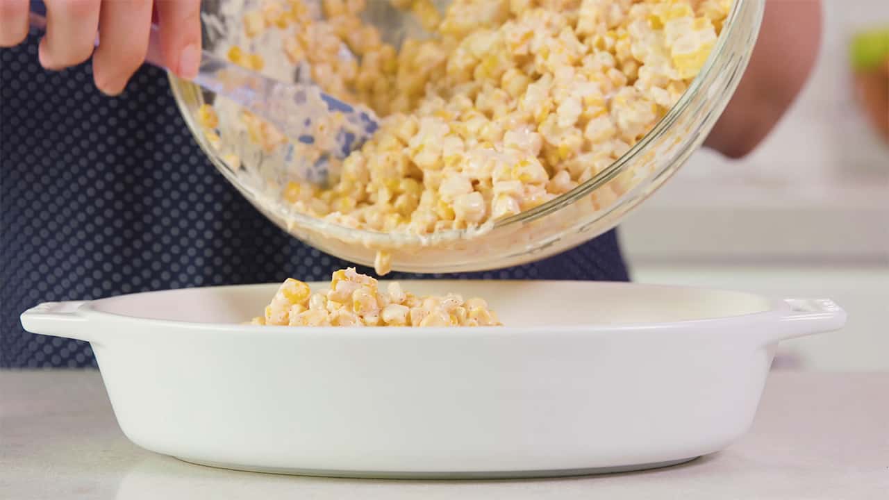 Evacuate ingredients from mixing bowl into a white serving dish using spatula.