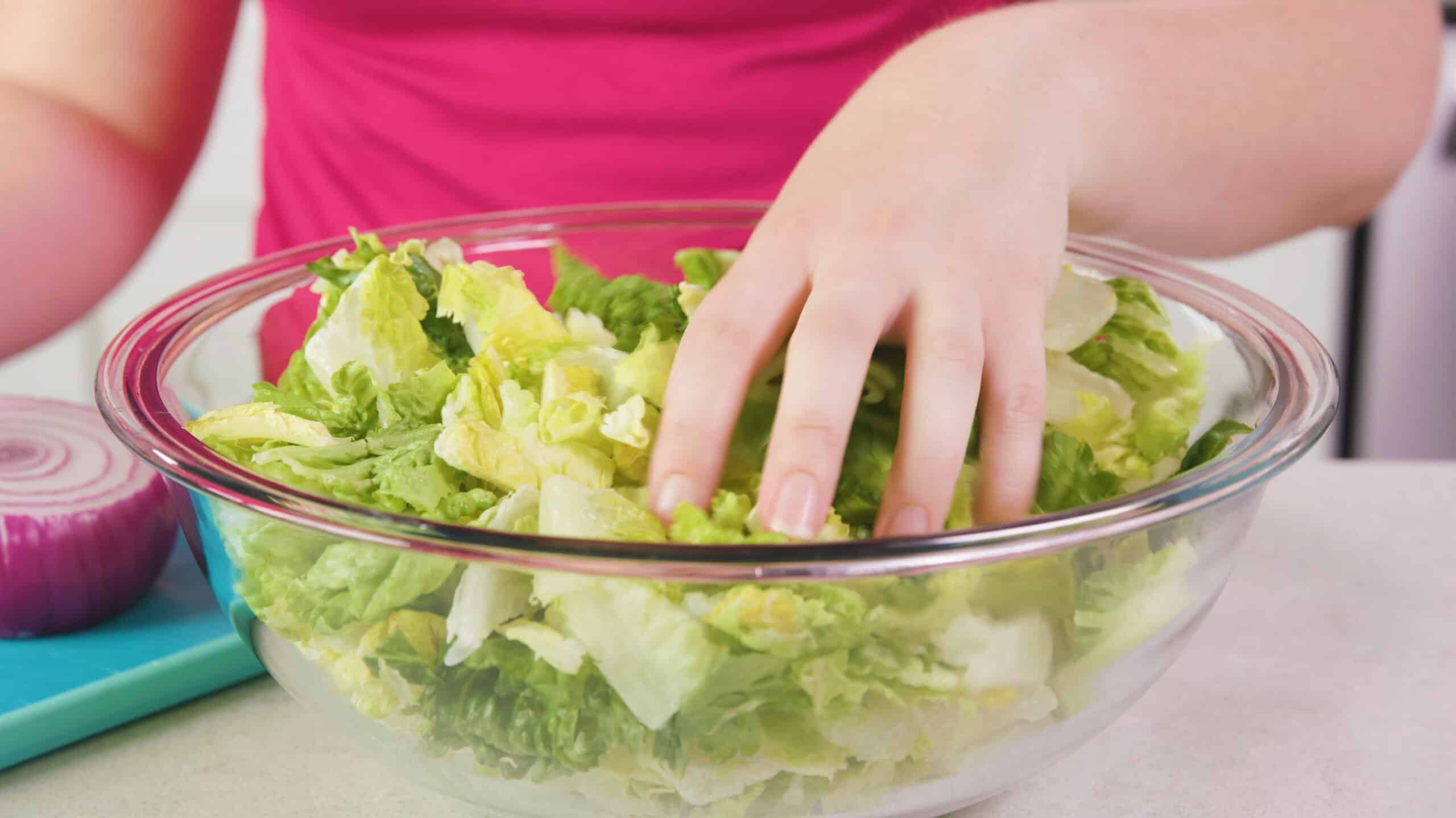 Angled view of a large clear glass mixing bowl filled with chopped green Romaine lettuce leaves.