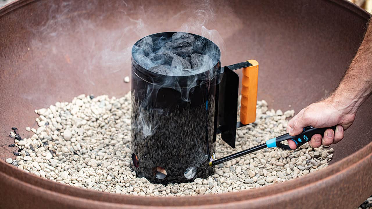 A Charcoal starter is lit with a lighter in a large fire pit