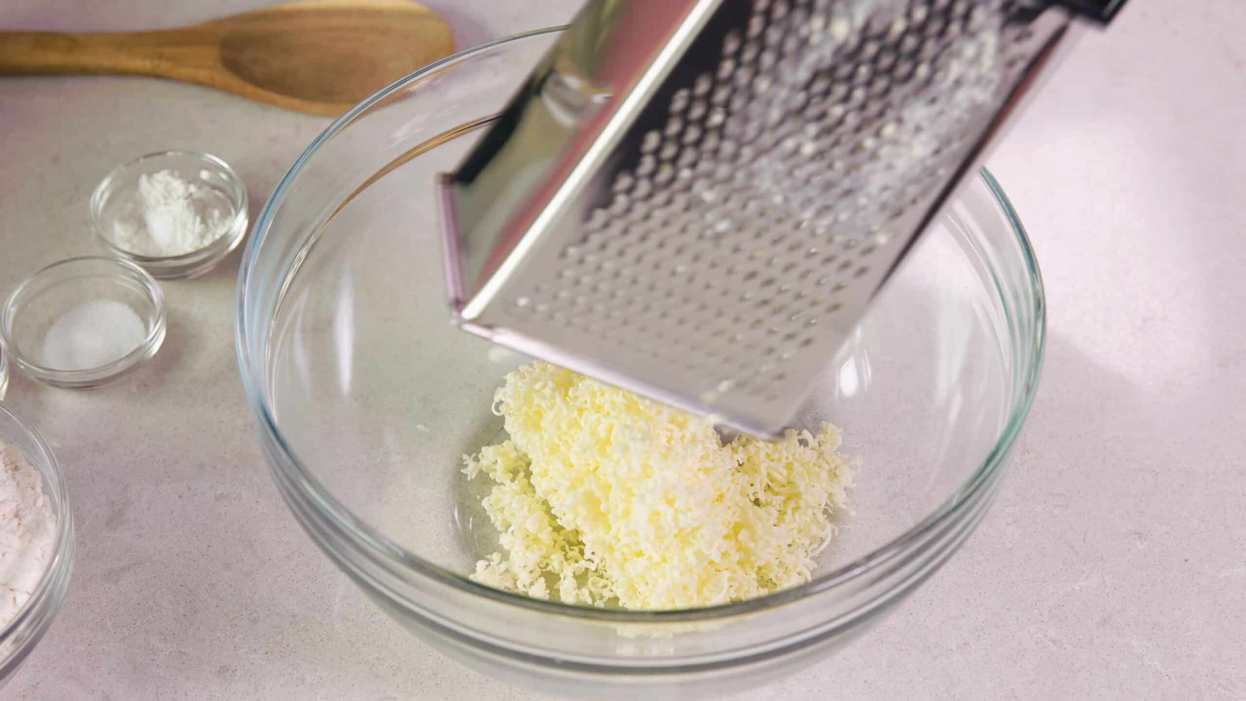 Using the fine side of a cheese shredder, shred required stick of cold butter into a mixing bowl to create fine sized shreds of butter to integrate into the biscuits.