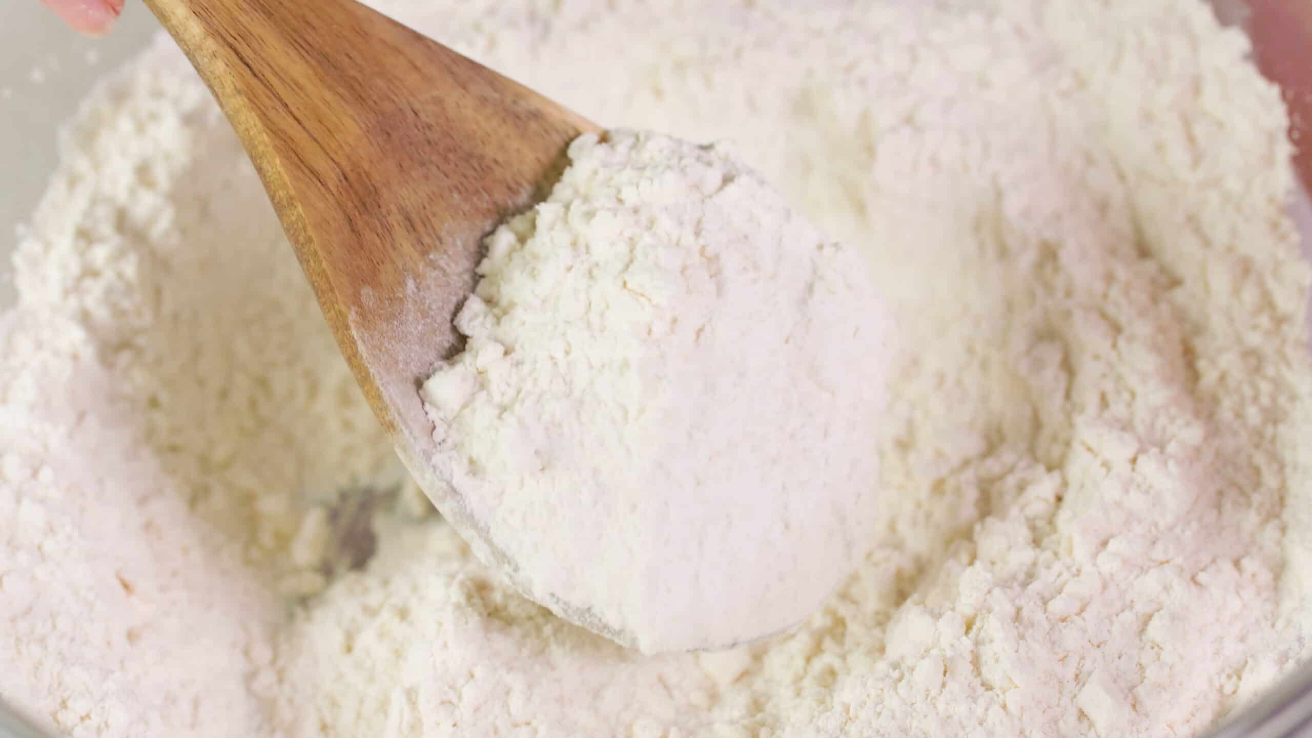 Close-up view of a wooden spoon with a portion of the mixed ingredients inside a mixing bowl to show the desired texture of the ingredients which is similar to damp sand.