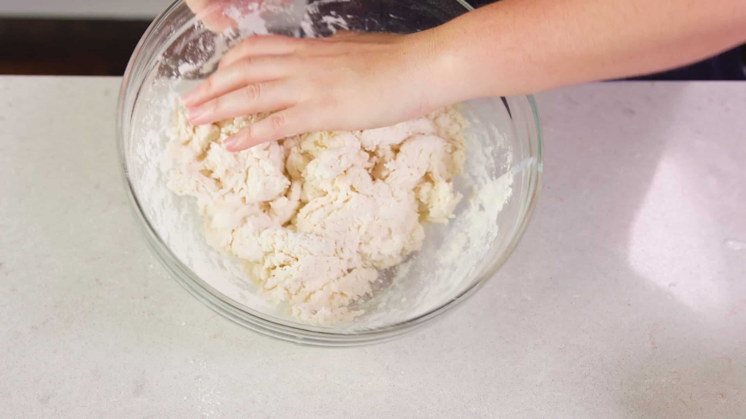 A mixing bowl filled with buttermilk biscuit dough is tipped ready to transfer the dough onto a clean countertop to knead.