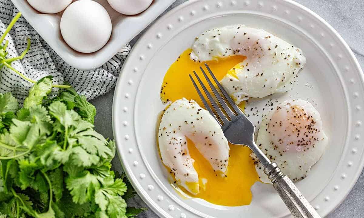 A bird's eye view of Poached Eggs, seasoned with salt and pepper, with runny yolks after being cut into with a fork.