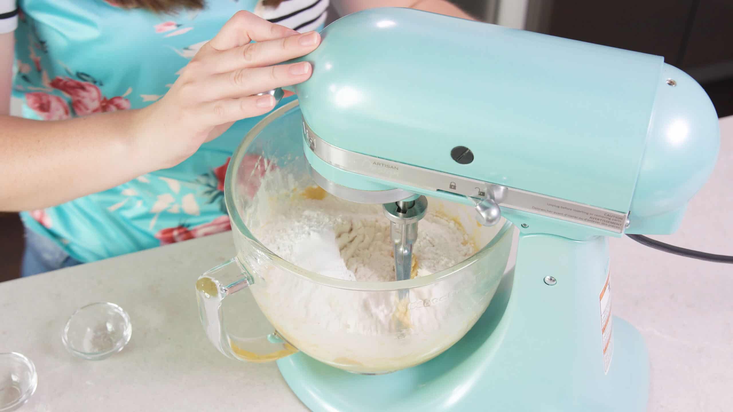 Angled view of countertop kitchen mixer with a clear glass mixing bowl filled with dry and wet ingredients for cookie dough.