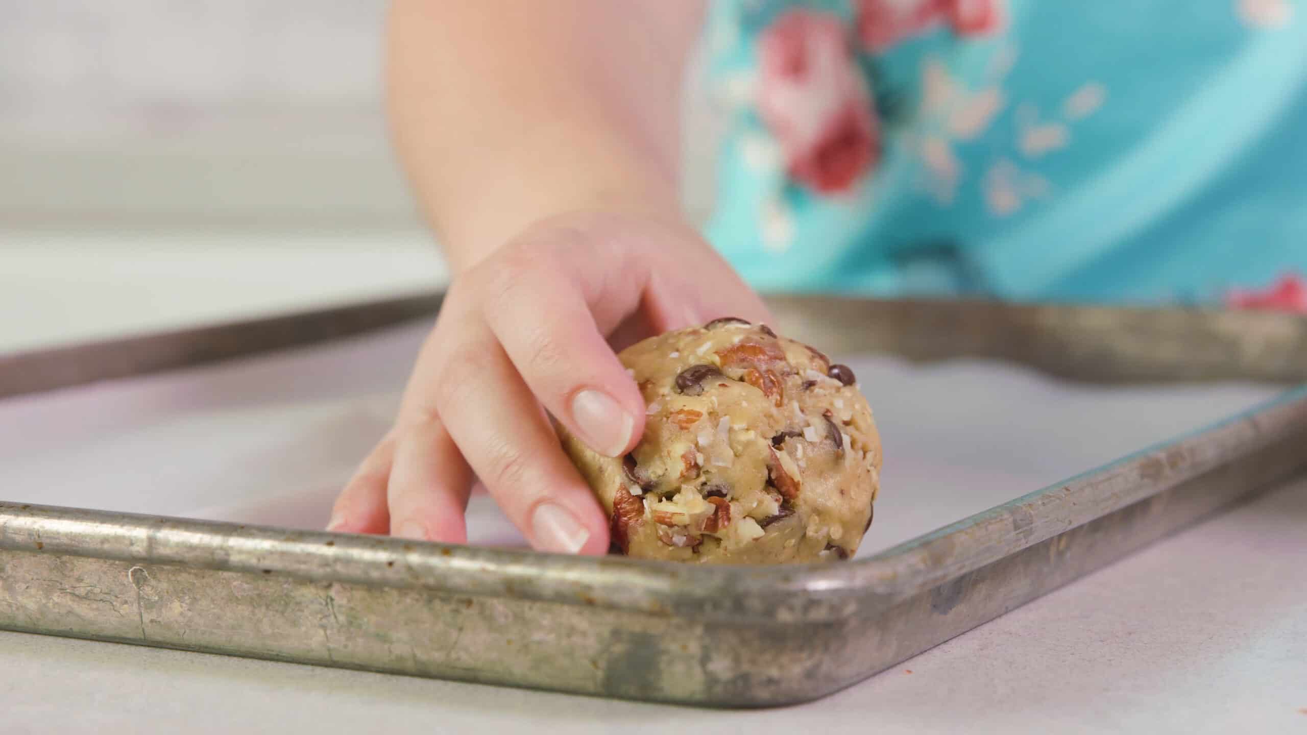 Side view of a metal baking sheet lined with parchment paper and a cowboy cookie dough ball placed on top.