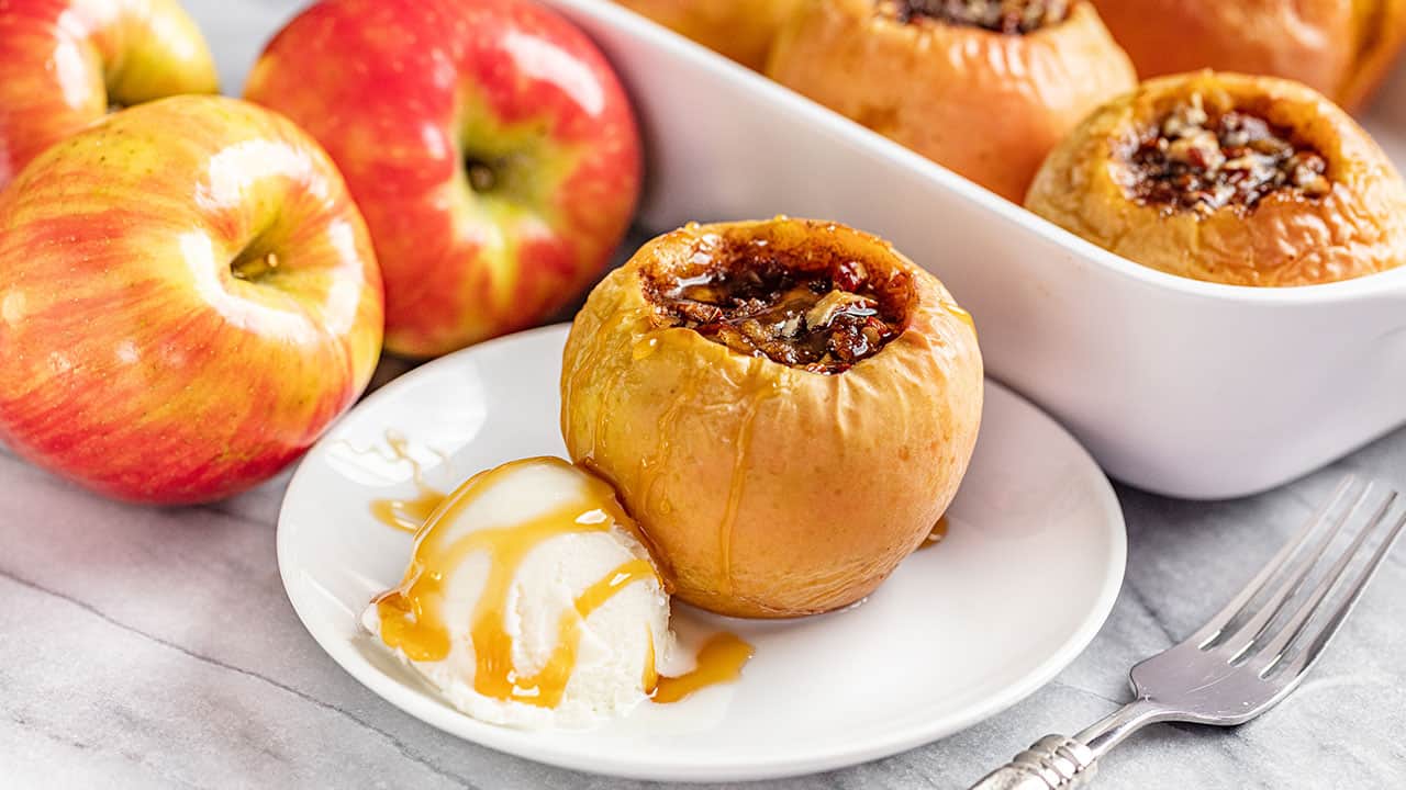 Classic Baked Apples are the perfect dessert for Fall. They are easy to make and are perfect for topping off with a scoop of vanilla ice cream. Baked Apple with a scoop of Ice Cream with a white dish full of baked apples in the background.