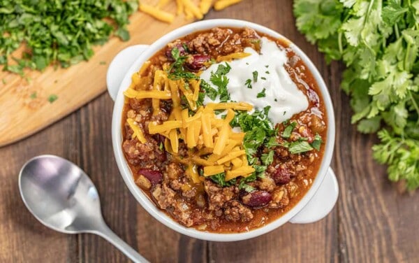 Chili topped with shredded cheese, cilantro and sour cream in a white soup bowl