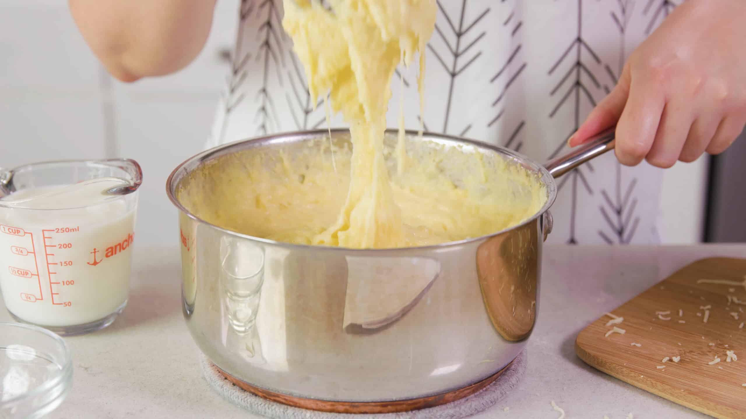 Side view of silver pot on countertop showing the texture and consistency of the polenta after mixing in the cheese with the other ingredients.