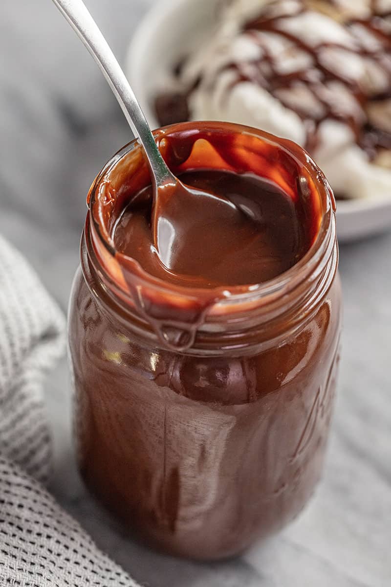 Mason jar full of hot fudge with a metal spoon in it.